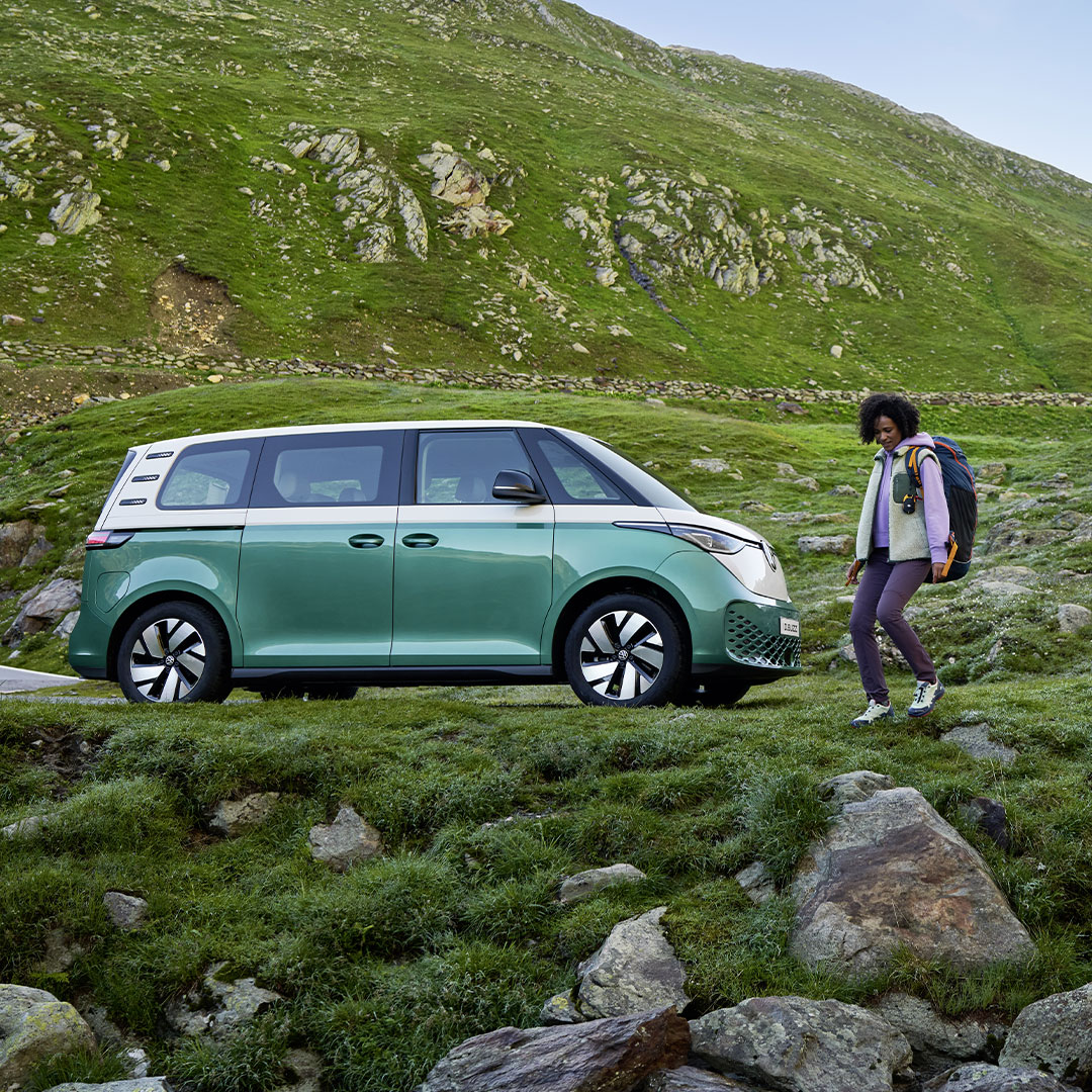 Una donna vicino al proprio Volkswagen ID. Buzz parcheggiato in una zona di montagna.
